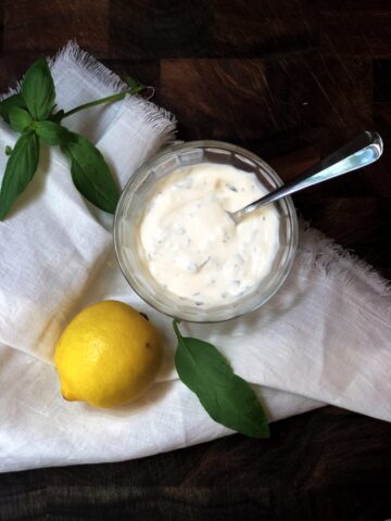 basil mayo in a bowl on a wood board with a lemon next to it.