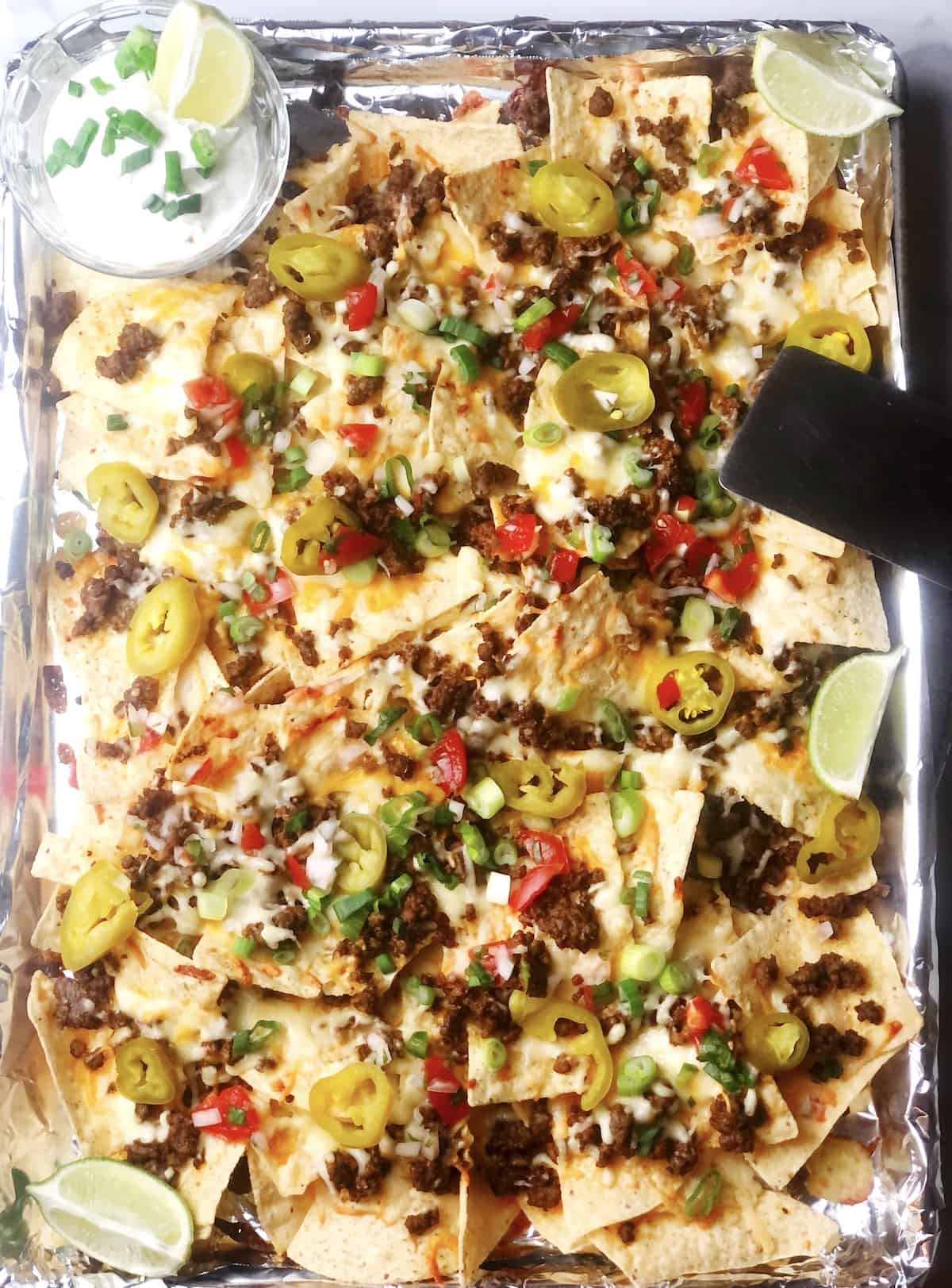 Loaded nachos on a sheet pan with toppings.