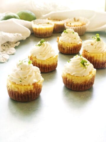 Mini Key Lime Cheesecakes with lime zest on a counter with Key limes in the background.