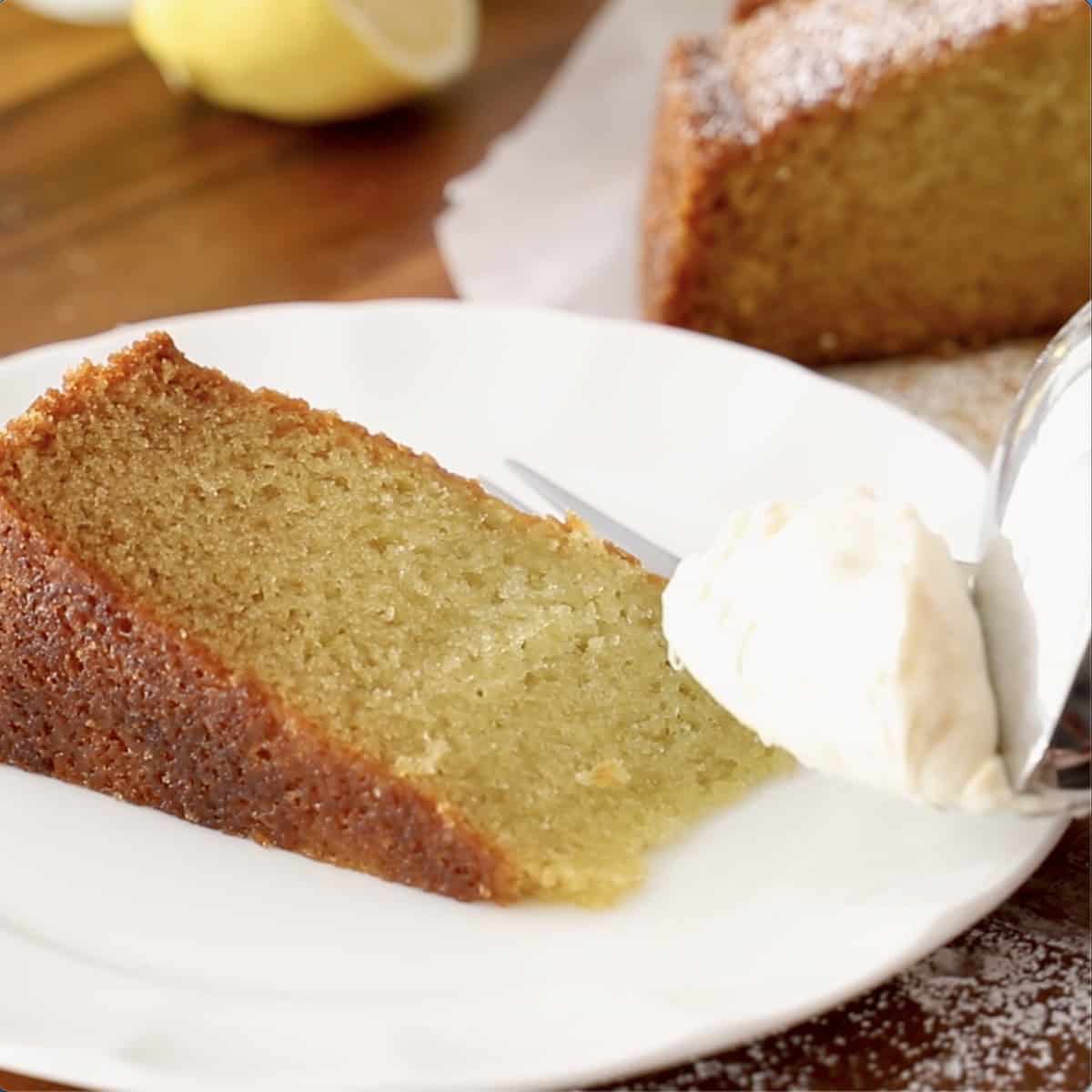 A slice of basil olive oil cake on a plate with whipped cream.