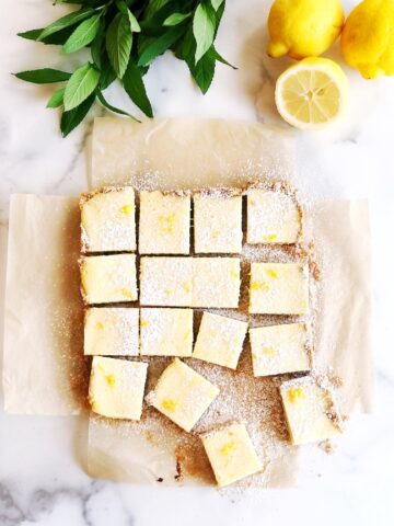 Sliced lemon bars on parchment paper with lemons next to it.