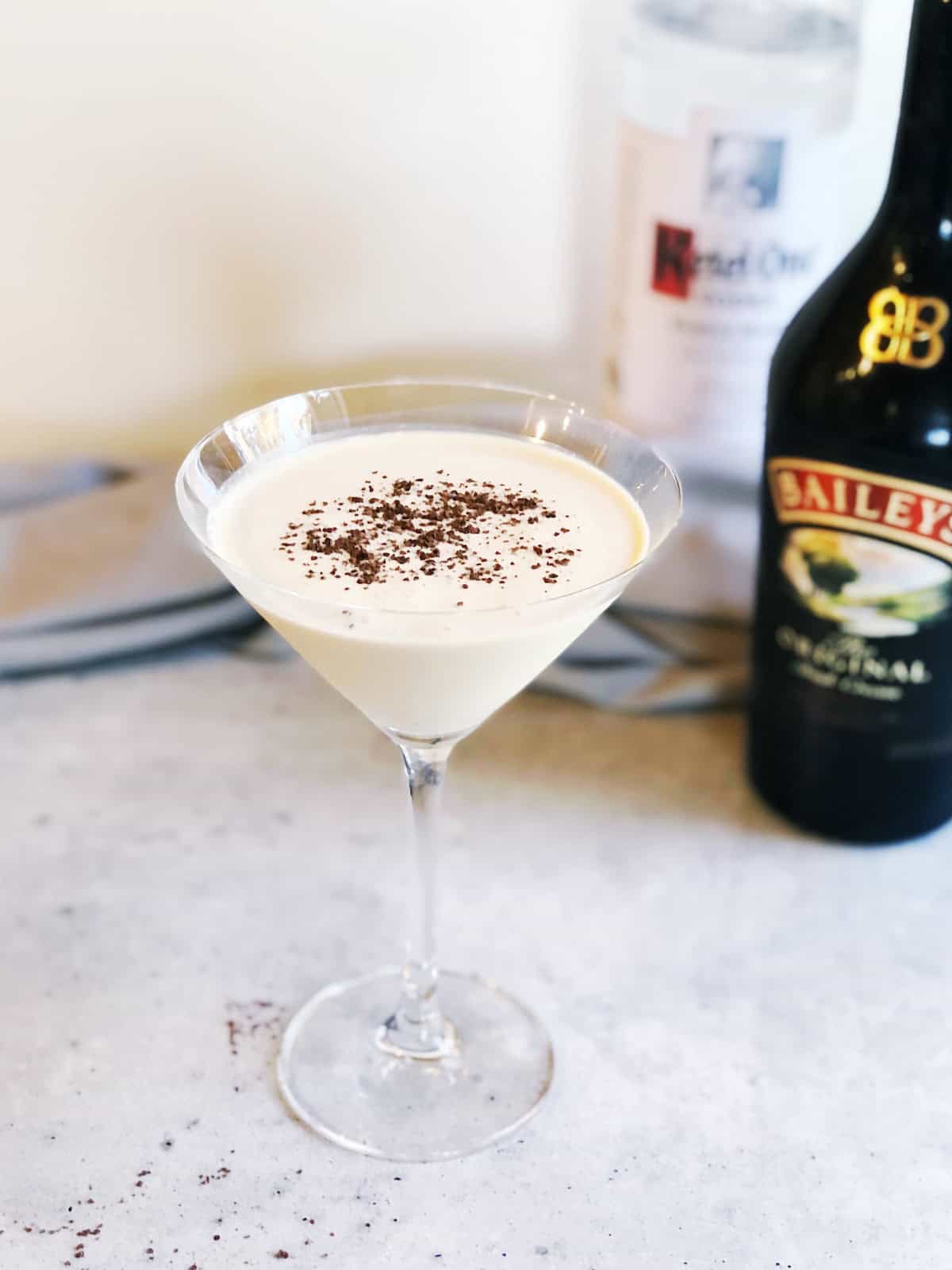 Baileys and vodka martini in a martini glass with the ingredients in the background.