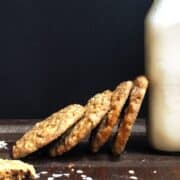 Oatmeal cookies stacked on their side on a wood board and leaning on a pint of milk.