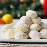 Snowball cookies piled up into a pyramid shape on a white plate with an orange and lemon in the background.