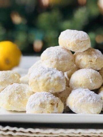 Snowball cookies piled up into a pyramid shape on a white plate with an orange and lemon in the background.