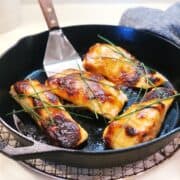 A zoomed in view of four baked miso salmon filets in a cast iron pan with a spatula in the pan and chives on top sitting on the counter.