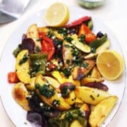 The roasted vegetables with green chimichurri sauce on top of them on a large oval plate with extra chimichurri sauce in a bowl in the background.