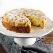The rustic Italian apple cake on a cake stand with a slice cut out of it.