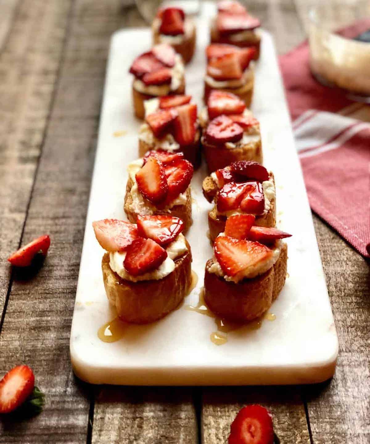 Crostini with goat cheese and balsamic strawberries on top on a long plate.