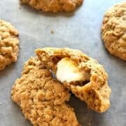 Oatmeal cookies stuffed with marshmallows on the counter with the cookie cut in half to show the marshmallow inside.