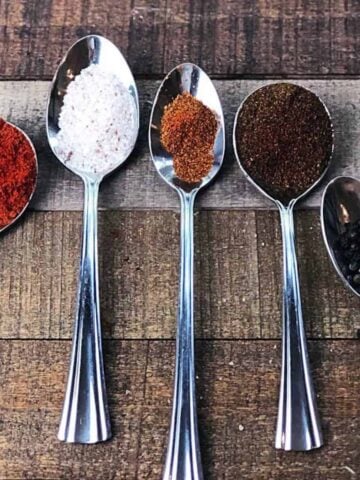 The different spices for the seasoning in individual silver spoons on a table.