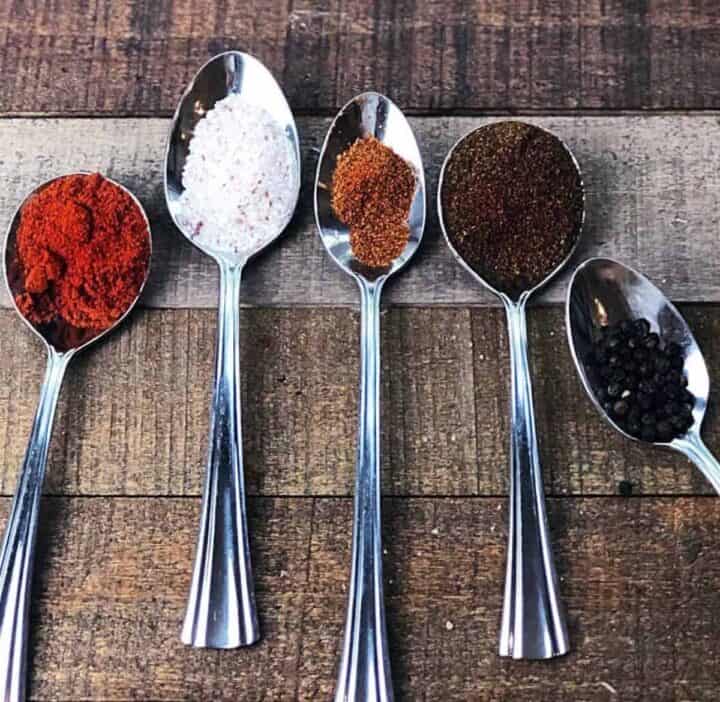 The different spices for the seasoning in individual silver spoons on a table.