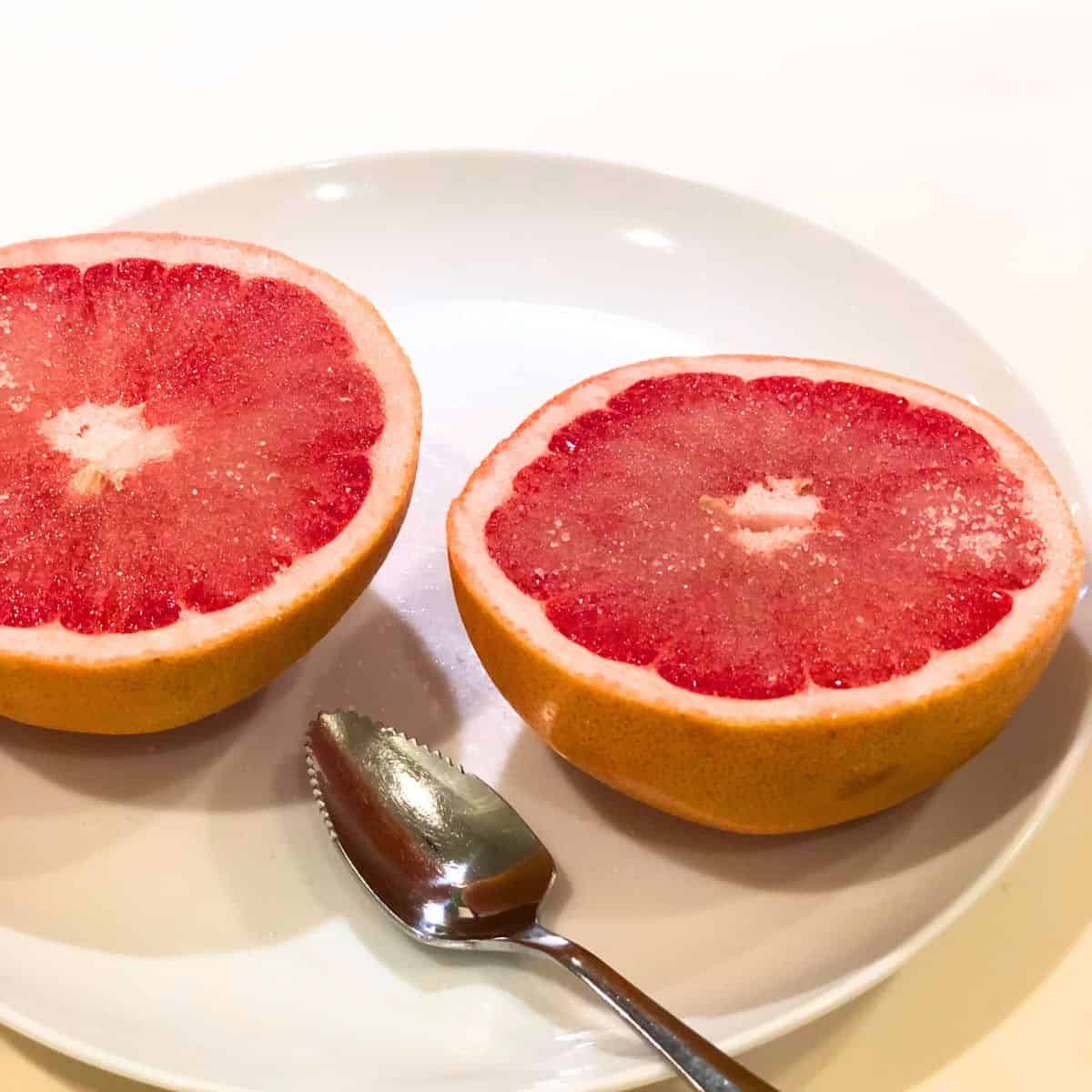 Grapefruit cut in half on a plate with sugar on top.